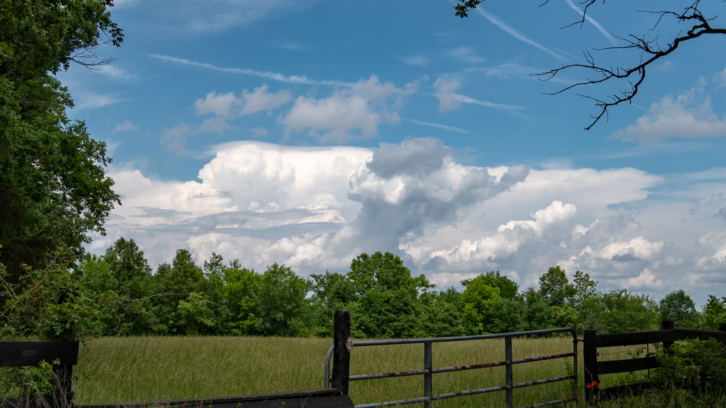 A photograph of a cumulonimbus calvus pileus velum cloud (Cb cal pil vel) over some farmland in Virginia